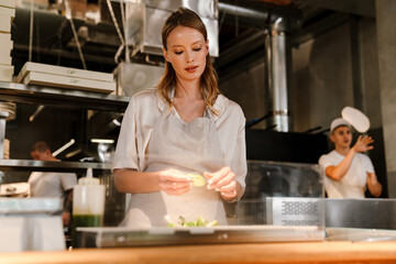 Young white chef woman cooking while working in restaurant kitchen