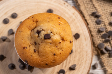 Muffin or cupcake with chocolate chips on wooden table background. Concept of making industrial or...