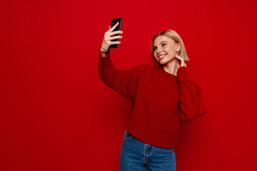 Young blonde woman smiling and taking selfie photo on cellphone