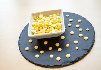 White chocolate flakes in a white ceramic bowl on a slate plate