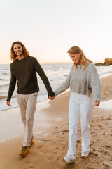 Smiling couple in love holding hands during walk at sunny beach