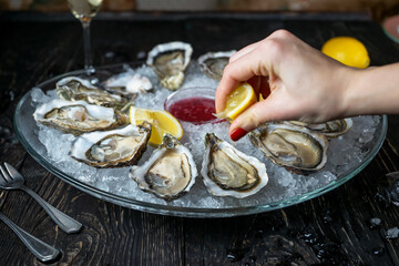 open oysters in a large plate with sauce and lemon sprinkled with lemon juice female hands macro
