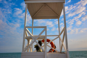 Lifeguard tower on the beach against the blue sky. Beach with a lifeguard tower and a lifebuoy, there is no lifeguard at the post. Wooden rescue tower by the sea