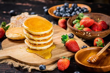 A bunch of pancakes with berries and honey. 