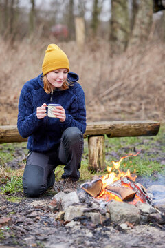 young woman by bonfire with hot chocolate in hand