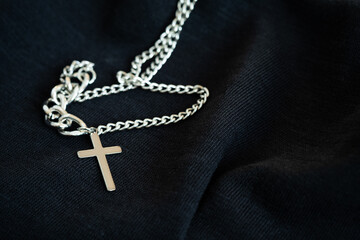 silver or stainless steel necklace with a cross pendant rests on a black cloth
