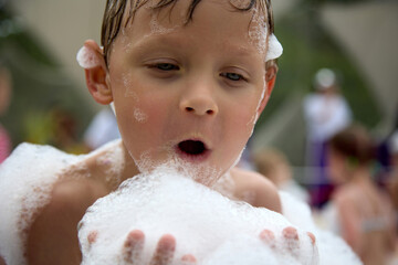 Close-up of the face of a cute little boy blowing a pile of white foam off his hands at a party....