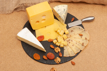 Different types of cheese on a black graphite board decorated with dried apricots and nuts