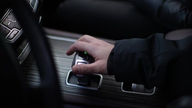 Close-up high-angle view of unrecognizable male car driver switching automatic transmission driving mode parking shift. Businessman driving expensive car. Driver in auto gear lever drive mode.