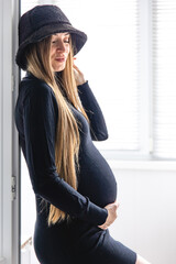 A pregnant woman with long hair in a black dress in the interior of the room.