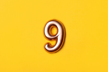 Metal number nine on a yellow background. Top view.