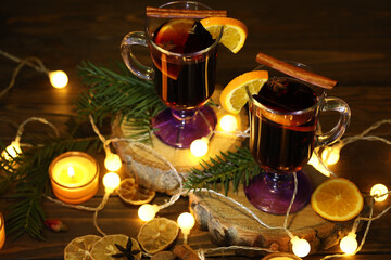 mug of mulled wine with decoration and candles on dark wooden background