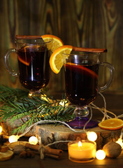 mug of mulled wine with decoration and candles on dark wooden background