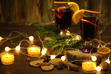 mug of mulled wine with decoration and candles on dark wooden background