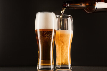 Pouring beer into glasses from bottle on dark.