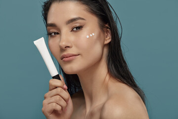 Brunette girl with three drops of cream, moisturizer on her cheek.