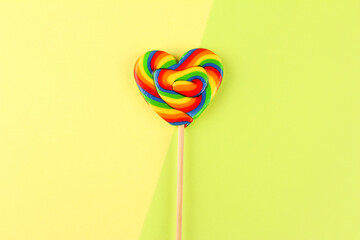 Rainbow colored heart shaped lollipop on yellow and green background