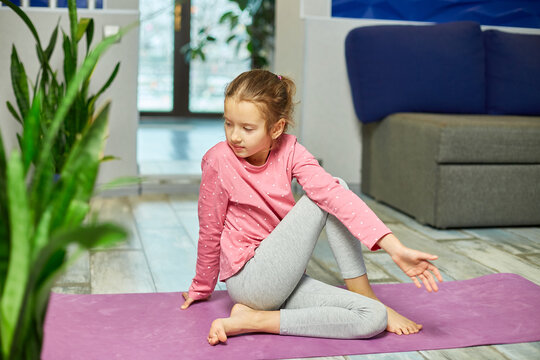 Little girl doing stretching exercises, practicing yoga on fitness mat at home