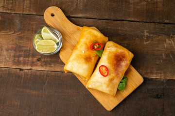 Chimichanga or burrito on a wooden table, top view.