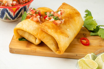 Traditional chimichanga two pieces, Mexican delicious cuisine. Chmimichanga lies on a wooden board with chili pepper next to salsa sauce.