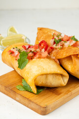 Chimichanga with salsa sauce, Mexican traditional cuisine. Light background, vertical photo