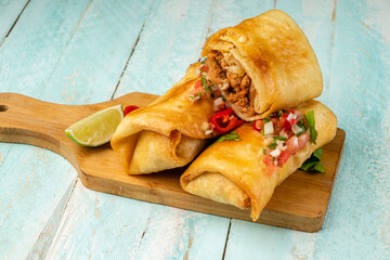 Chimichanga is a traditional Mexican fast food on a wooden board, one cut inside minced meat and...
