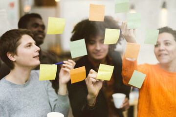 young team of diverse people working with passion on sticky post on window finding new strategy -...