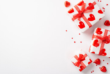 Valentine's Day concept. Top view photo of gift boxes with red ribbon bows heart shaped candies and sprinkles on isolated white background with copyspace