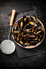 Full bowl with boiled mussels on a stone board. 
