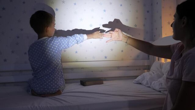 Cute boy with mother in pajamas playing with shadows on wall from hte flashlight. Family having time together, parenting, happy childhood and entertainment