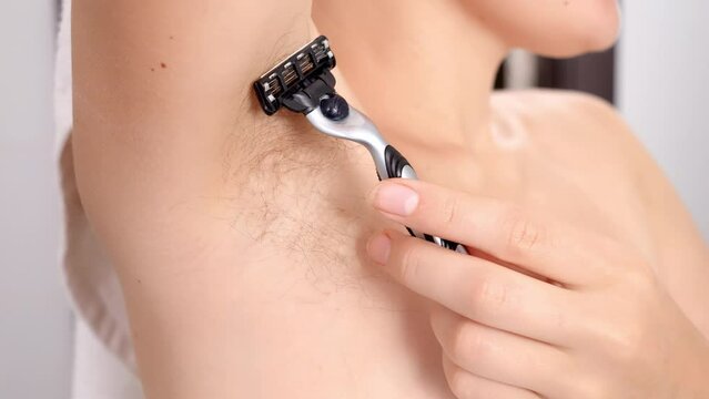 Closeup of woman with long armpit hair shaving and using razor in bath. Concept of hygiene, natural beauty, feminity and body hair growth