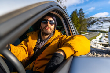A man inside a gray car on a snowy hill in winter, enjoying driving