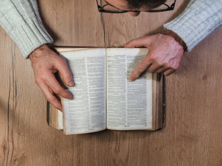 Naklejka premium Caen, France 2023. Man reading an old book top view, wooden table