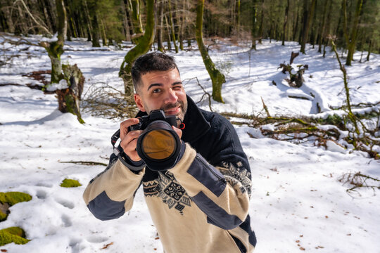Photographer man taking a picture in the snow, enjoying winter photography in a beech forest