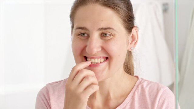 Portrait of happy smiling woman standing in bathroom and checking her mouth and teeth. Concept of teeth health, self checking mouth and oral hygiene