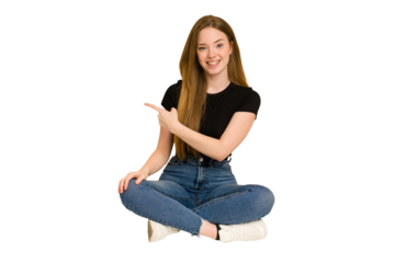 Young redhead woman sitting on the floor cut out isolated smiling and pointing aside, showing something at blank space.