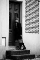 A sad woman on the porch of the house knocks on the door. Black and white photo.