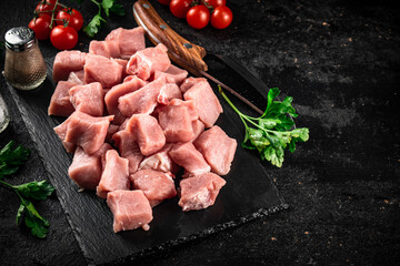 Pieces of raw pork on a stone board with parsley, tomatoes and spices. 