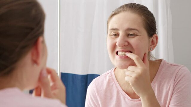 Beautiful smiling woman looking at her reflection in mirror and rubbing off the tooth plaque. Concept of teeth health, self checking mouth and oral hygiene