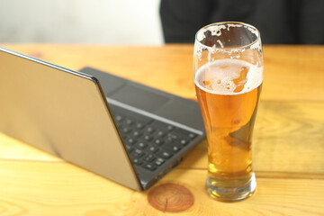 a pint with beer on the table next to the laptop and a person