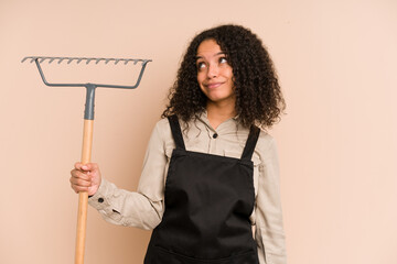 Young african american gardener woman holding a rake isolated dreaming of achieving goals and...