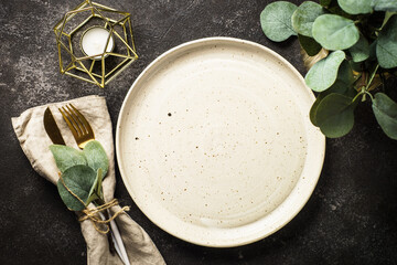 White craft plate, cutlery, wine glass and eucaliptus at black stone table. Top view image.