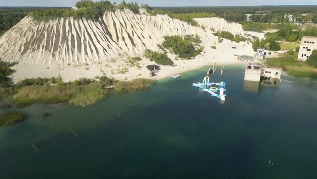 Crystal clear light blue lagoon of Rummu quarry and the adjacent ash hill. Drone shot of white sand mountain by the construction site. Beautiful white sand beach bathed by a turquoise water.