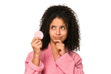 Young african american woman wearing a pink bathrobe holding a cellulose disk looking sideways with...