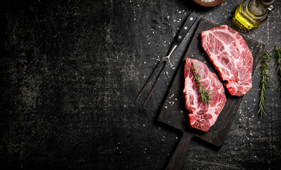 Raw pork steak on a cutting board with rosemary. 