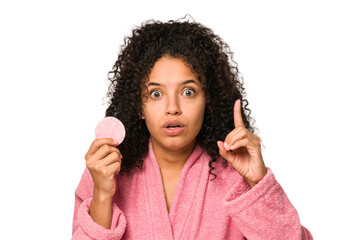 Young african american woman wearing a pink bathrobe holding a cellulose disk having an idea,...