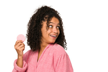 Young african american woman wearing a pink bathrobe holding a cellulose disk looks aside smiling,...