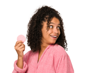Young african american woman wearing a pink bathrobe holding a cellulose disk looks aside smiling, cheerful and pleasant.