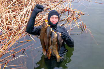 Fisherman with a trophy. Spearfishing, men in a neoprene wetsuit in a lake with weapons for...