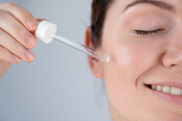 Caucasian woman uses blue anti-wrinkle face serum.